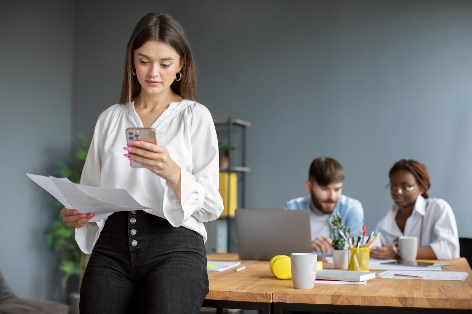 Mujer viendo el telefono en el trabajo con personas de fondo
